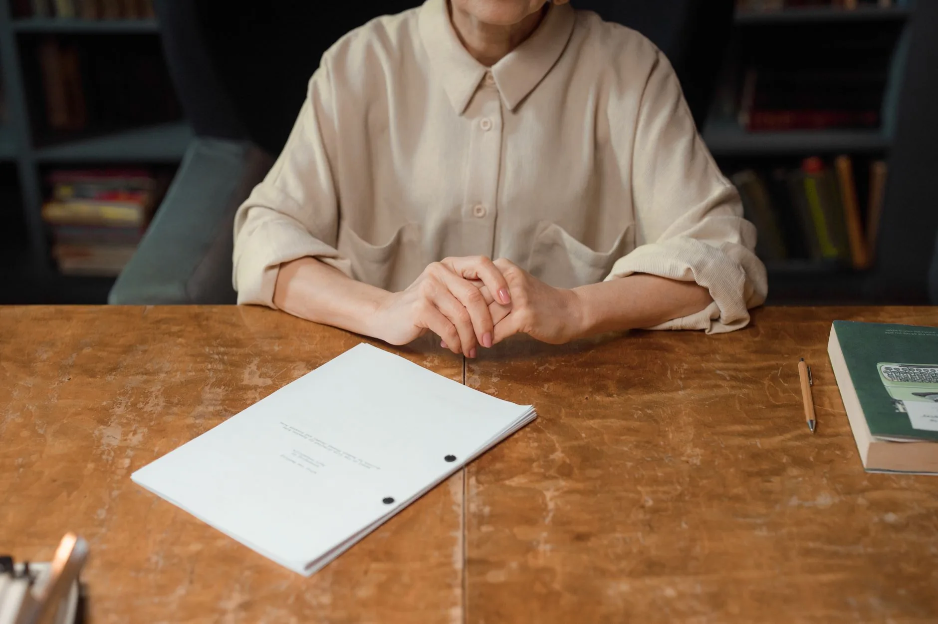 A cluttered mid-century desk under soft, diffused light, third person perspective, writing tools visible.
